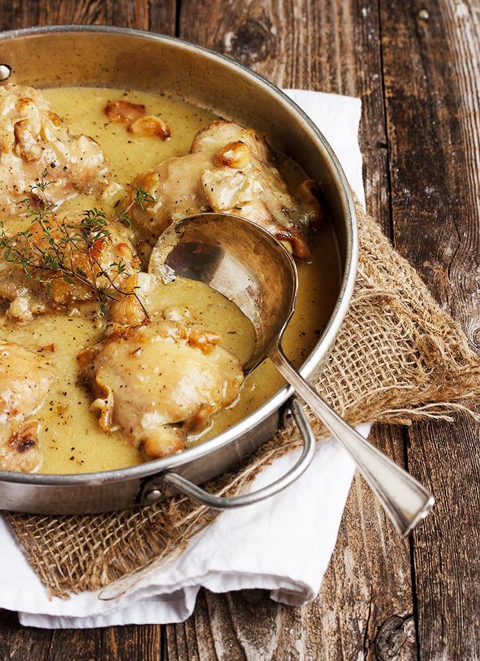 a pan filled with chicken and gravy on top of a wooden table next to a spoon