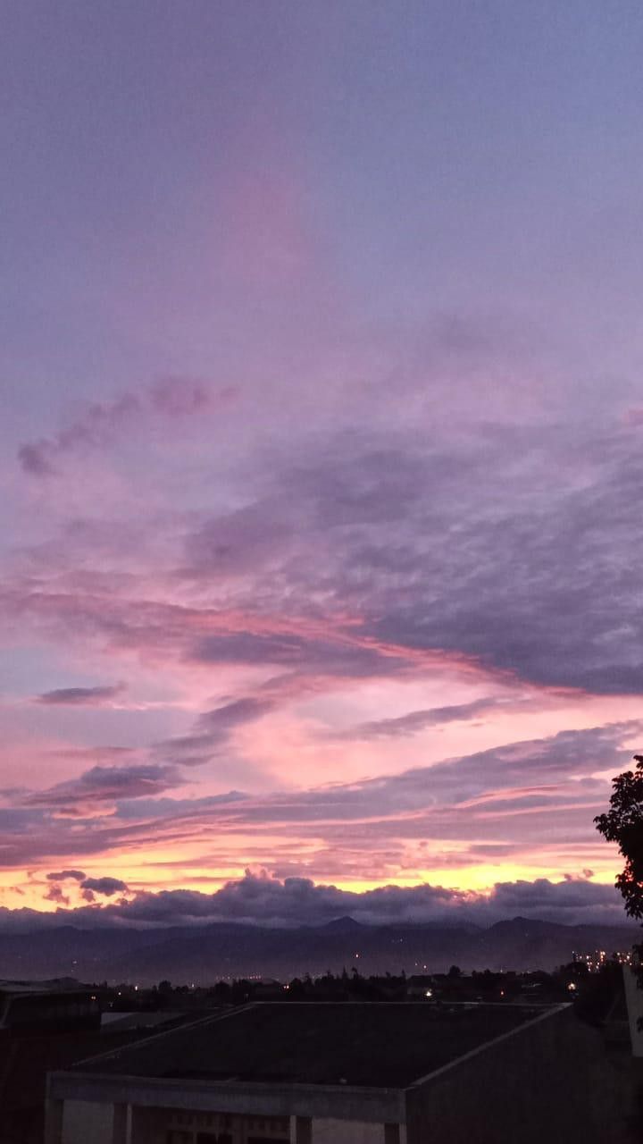 the sky is purple and pink as the sun sets in the distance behind some buildings