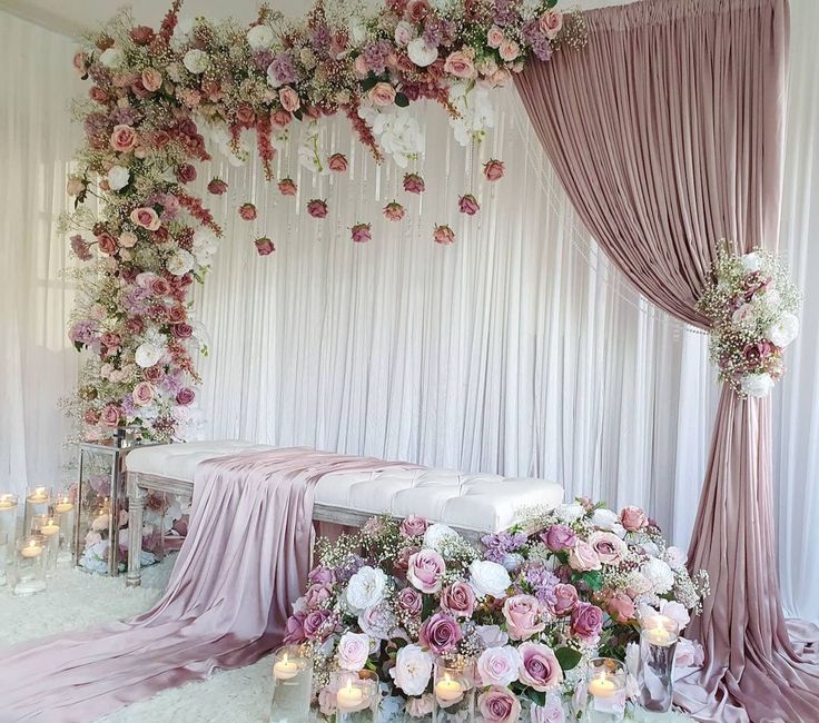 a white bench covered in flowers next to candles and draping on the wall