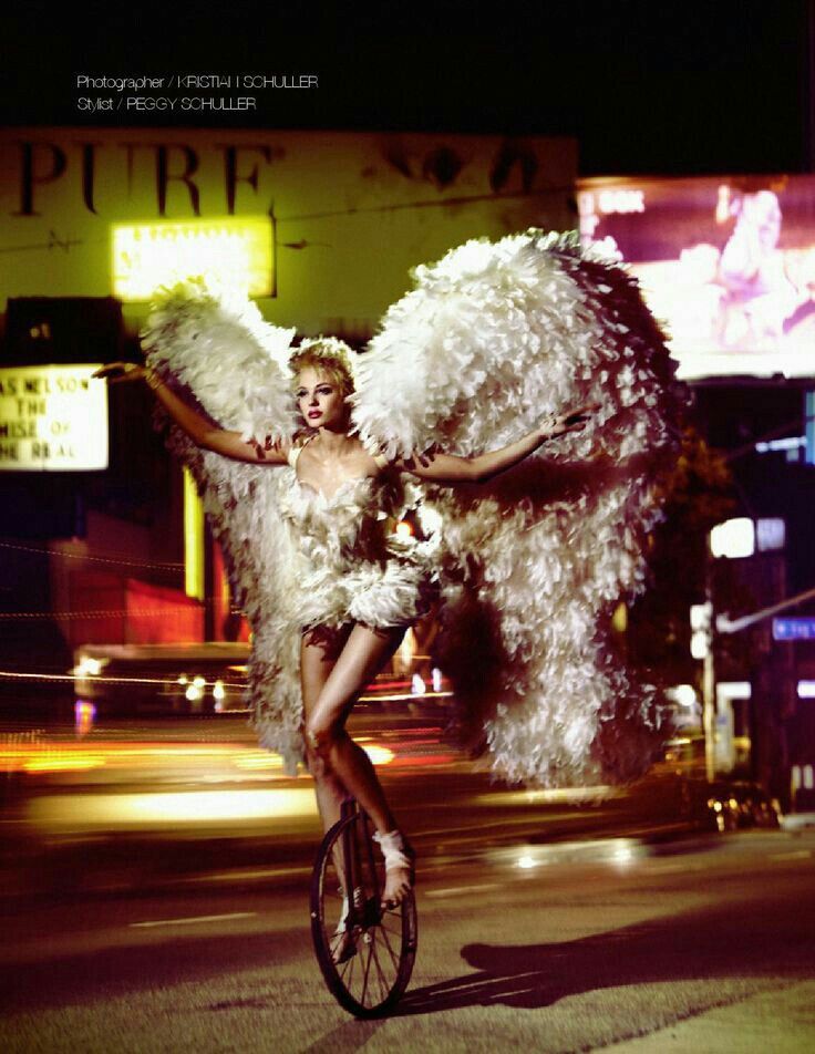 a woman on a unicycle posing in front of a giant bird costume