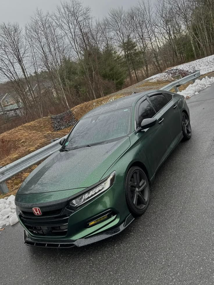 the green car is parked on the side of the road in front of some trees