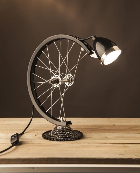 a bicycle wheel lamp on top of a wooden table next to a black light bulb