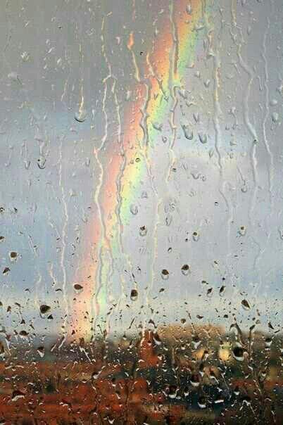 a rainbow is seen through the rain covered window