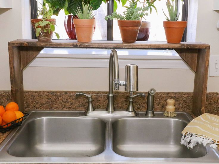 a kitchen sink under a window with potted plants on the ledge above it and oranges below