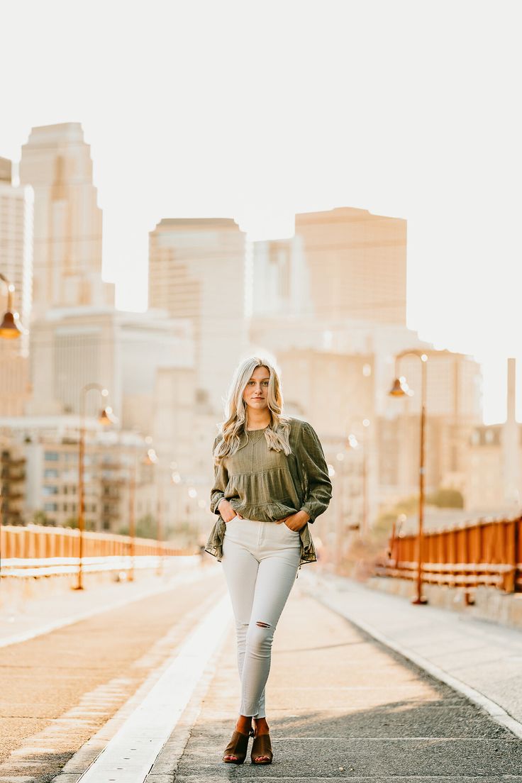 a woman standing on the sidewalk in front of a cityscape with her hands in her pockets