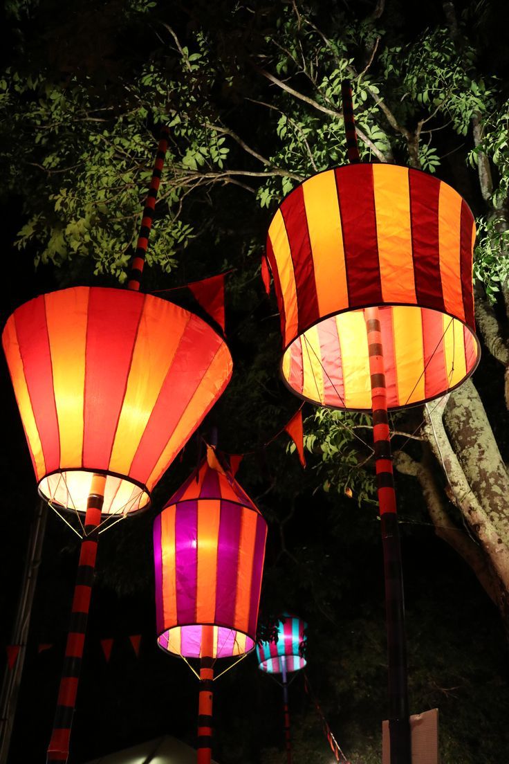 three brightly colored lanterns are lit up in the night sky, with trees behind them