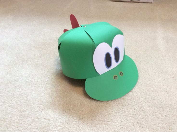 a green paper toy with eyes on it's face, sitting on the floor