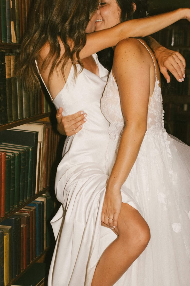 two brides hugging each other in front of bookshelves