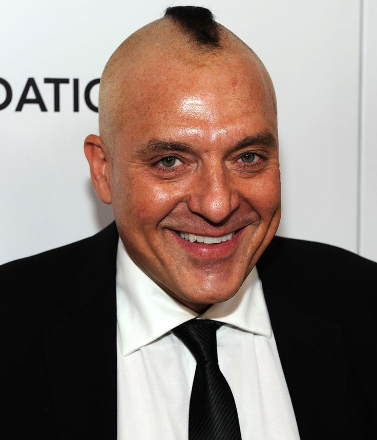 a bald man in a suit and tie smiling at the camera with his head tilted to the side