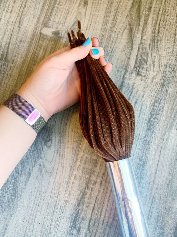 a woman's hand holding a hair brush on top of a wooden table next to a piece of cloth