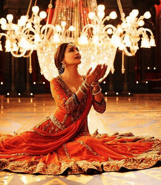 a woman in an orange dress sitting on the floor with her hands together and praying