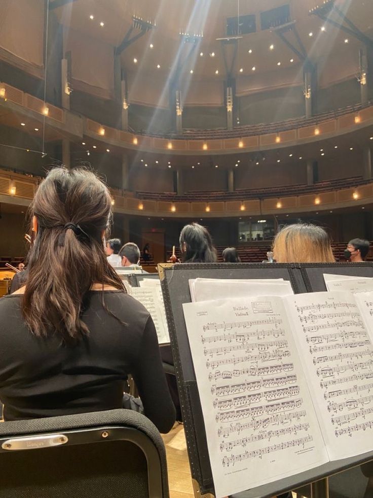 two women sitting in chairs with sheet music on their laps and an orchestra behind them