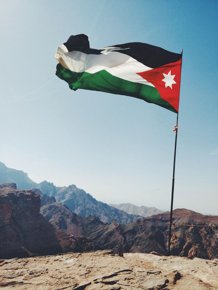 a flag flying high in the sky on top of a rocky mountain range with mountains in the background