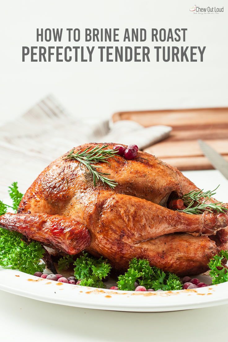 a roasted turkey on a plate with herbs and cranberries in the foreground text reads how to brine and roast perfectly tender turkey