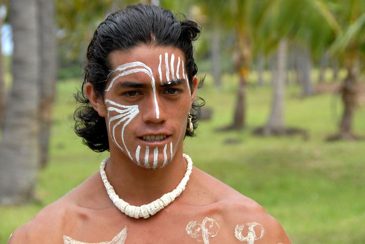 a man with white paint on his face and chest standing in front of palm trees