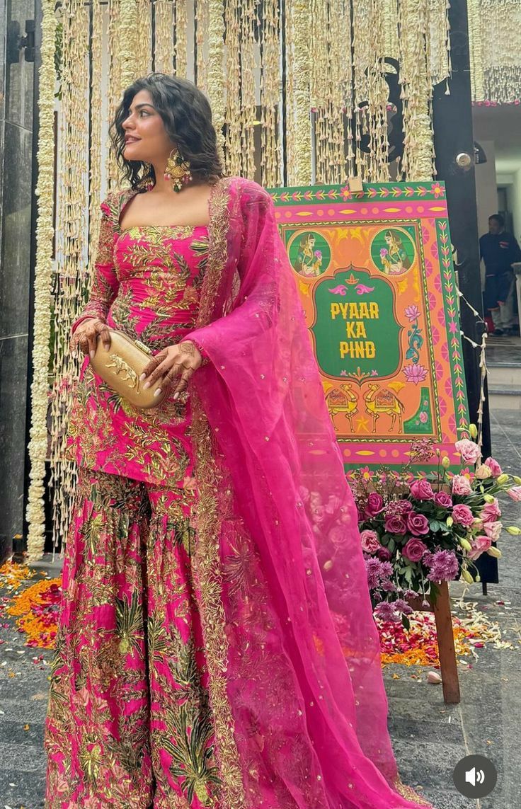 a woman in a pink and gold outfit standing next to a sign with flowers on it