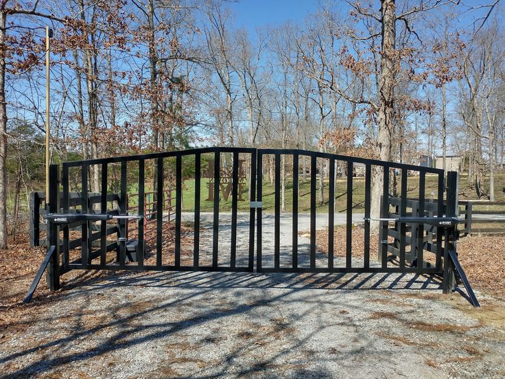 a black gate in the middle of a dirt area with trees and grass behind it