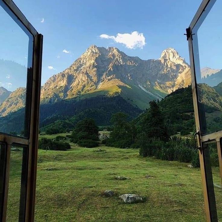 an open window looking out onto a grassy field with mountains in the distance and trees on either side