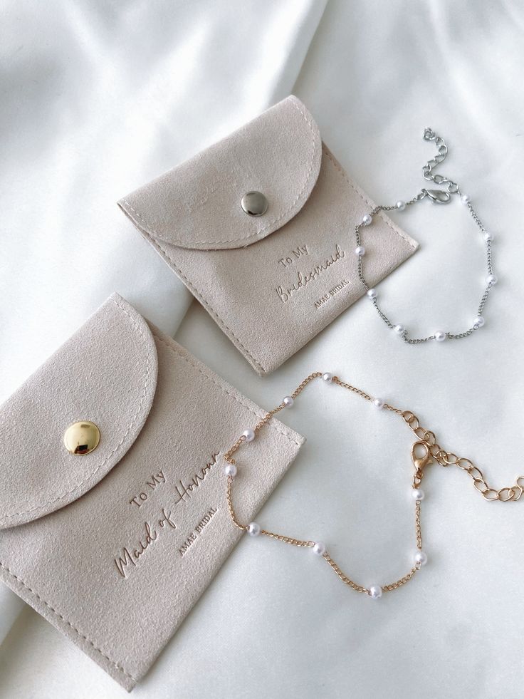 two white purses with personalized tags on them sitting on top of a bed