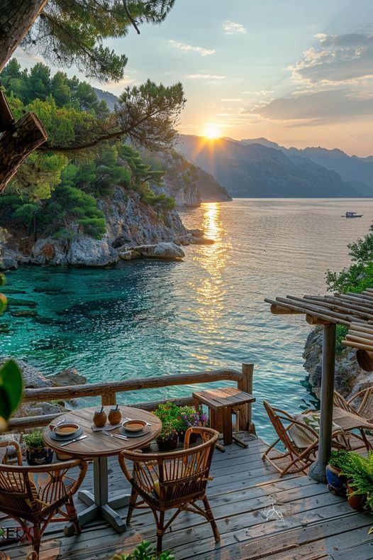 an outdoor dining area with wooden tables and chairs overlooking the ocean at sunset or sunrise