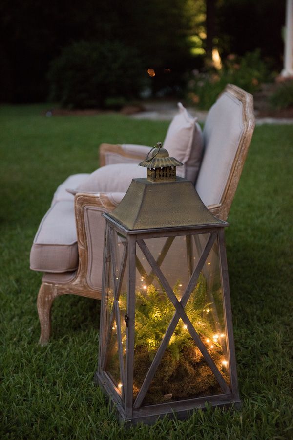 a chair sitting on top of a lush green field next to a light filled lantern