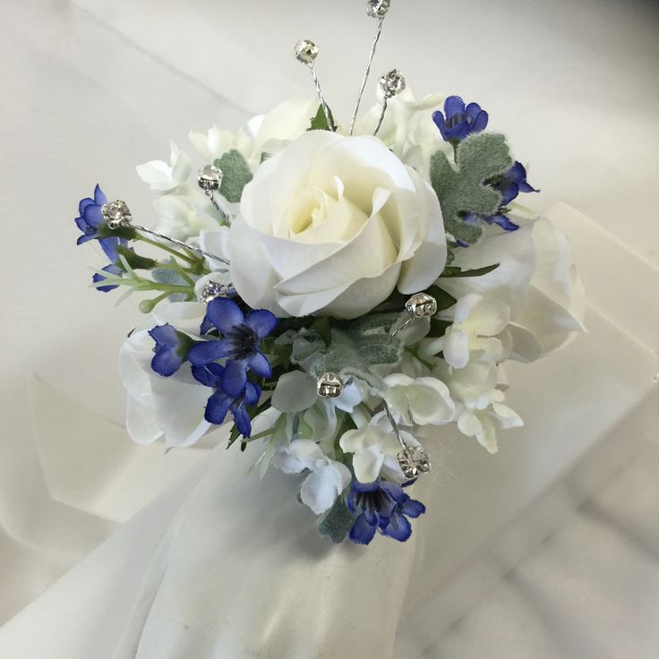 a bridal bouquet with white roses and blue flowers on a white satin material background