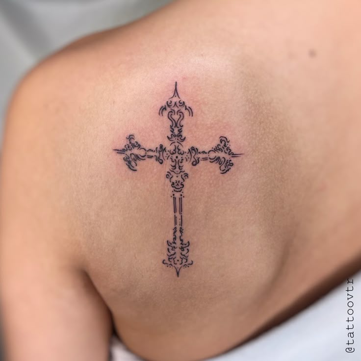 a cross tattoo on the back of a woman's shoulder