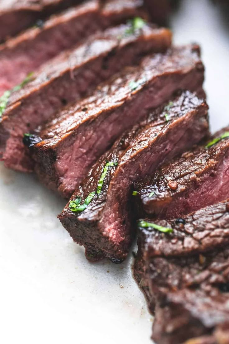 some meat is sitting on a plate with green garnish and seasoning around it