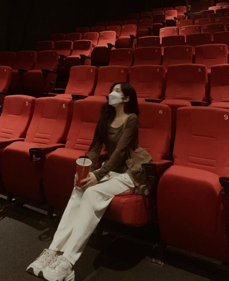 a woman sitting on a red chair with a cup in front of her and wearing a face mask