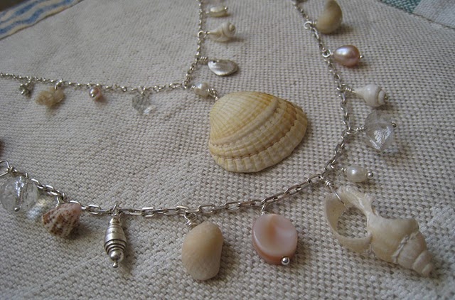 several seashells on a silver chain laying on a tablecloth with other sea shells