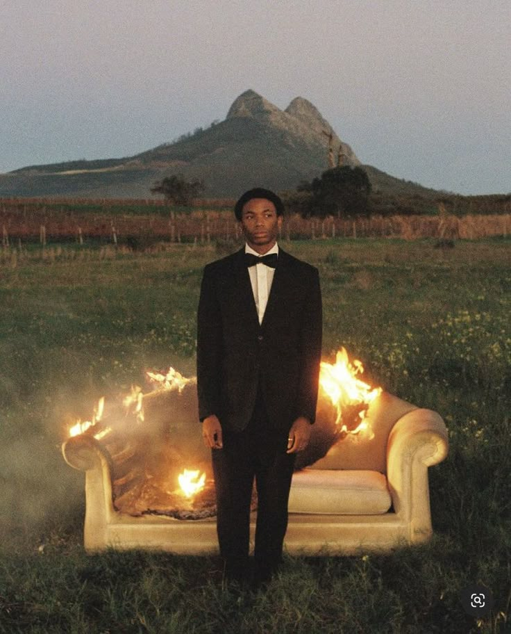 a man in a tuxedo standing next to a couch with flames on it