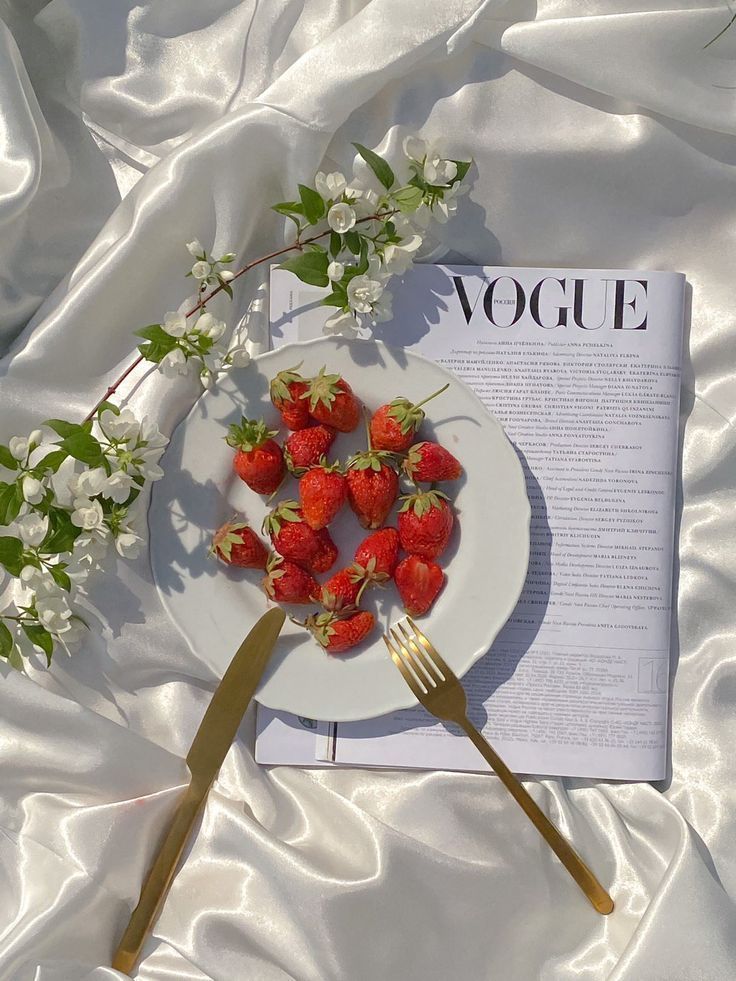 strawberries are arranged on a plate next to a fork and magazine with the word voge written in it