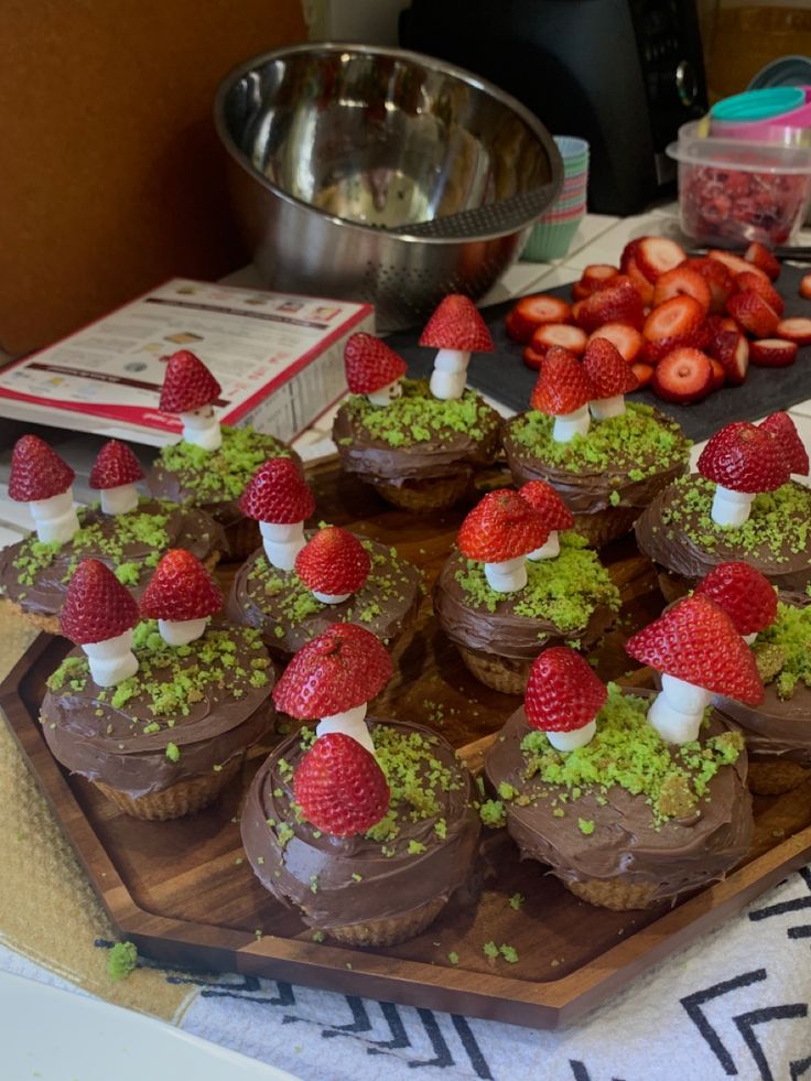 chocolate cupcakes topped with strawberries and green sprinkles on a wooden tray