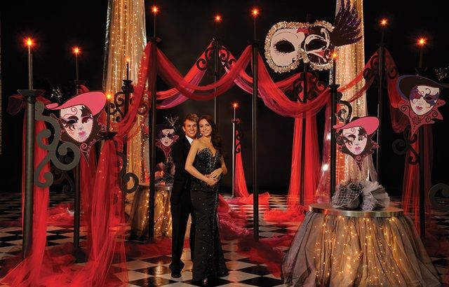 two women standing next to each other in front of red drapes and masks on display