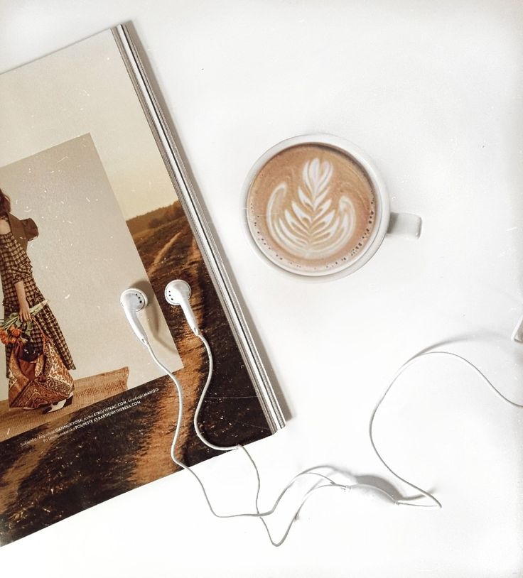 there is a cup of coffee and headphones next to the book on the table