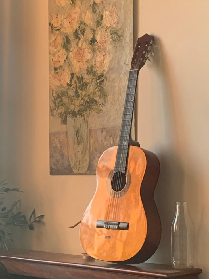 an acoustic guitar sitting on top of a wooden shelf next to a vase with flowers