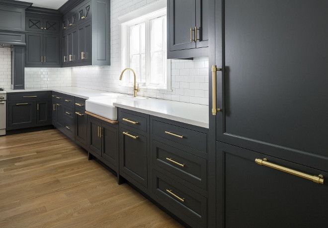 a kitchen with black cabinets and white counter tops, gold pulls on the cabinet doors