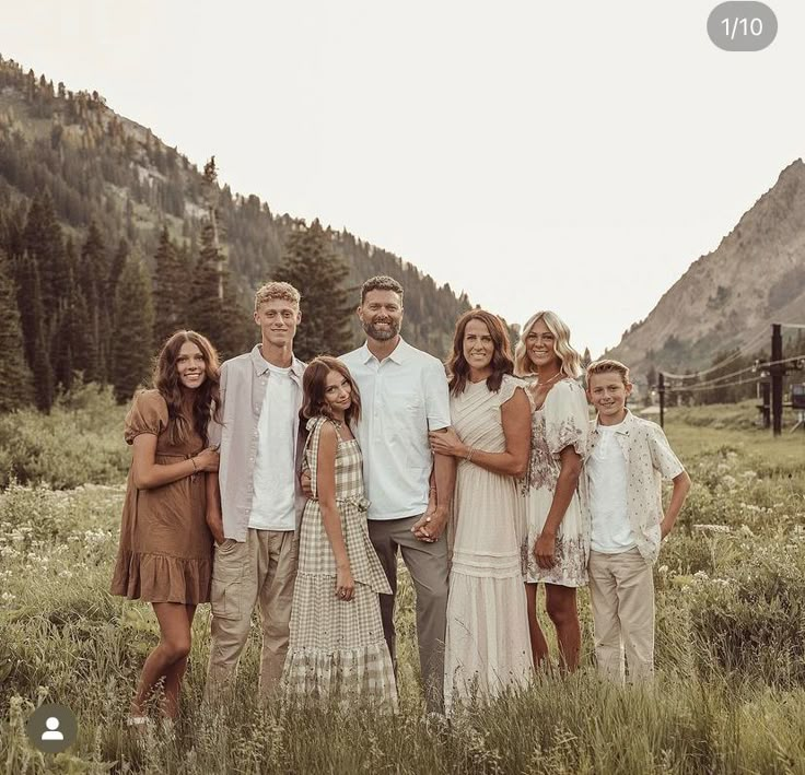 a family posing for a photo in a field with mountains in the background and trees behind them