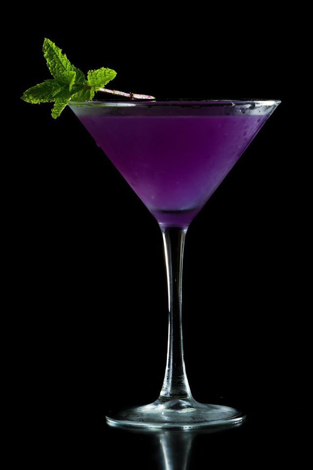 a purple drink in a martini glass with a green garnish