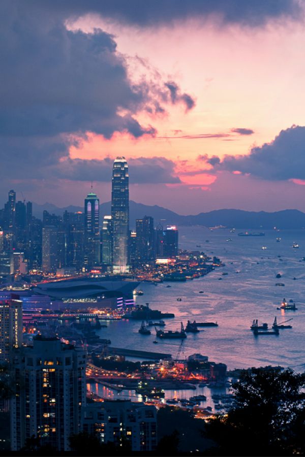 the city skyline is lit up at night with boats in the water and dark clouds