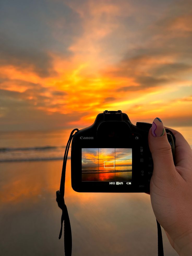 a person holding up a camera with the sun setting in the background