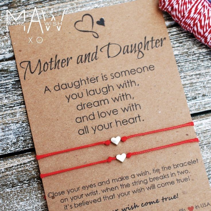 a mother and daughter bracelet on a card with red string attached to it, next to a spool of twine