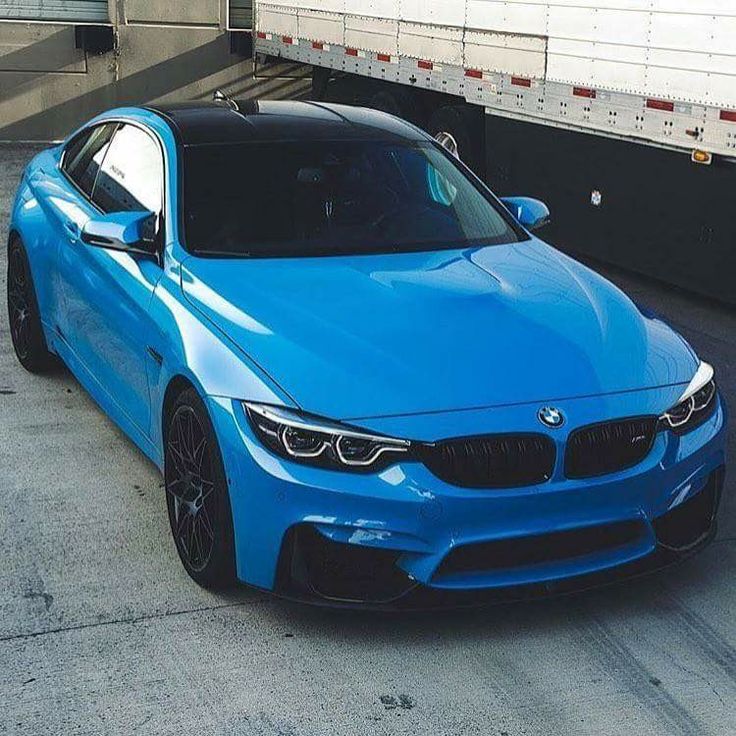 a blue bmw is parked in front of a semi - truck on the side of the road