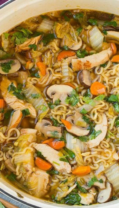 a pot filled with noodles and vegetables on top of a purple cloth next to chopsticks