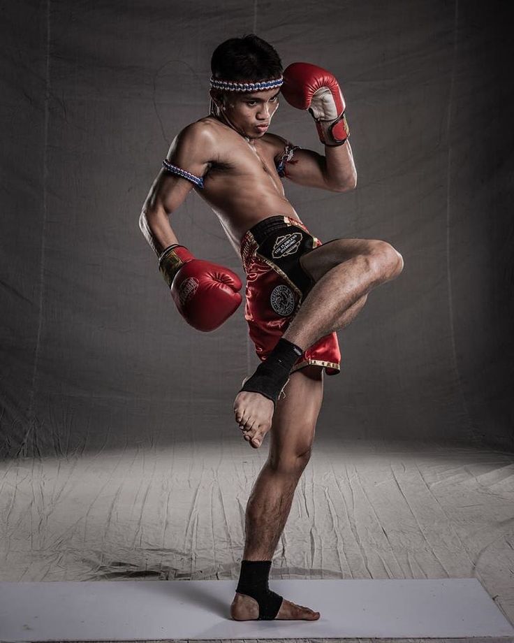 a man with boxing gloves on standing in front of a gray background wearing red shorts