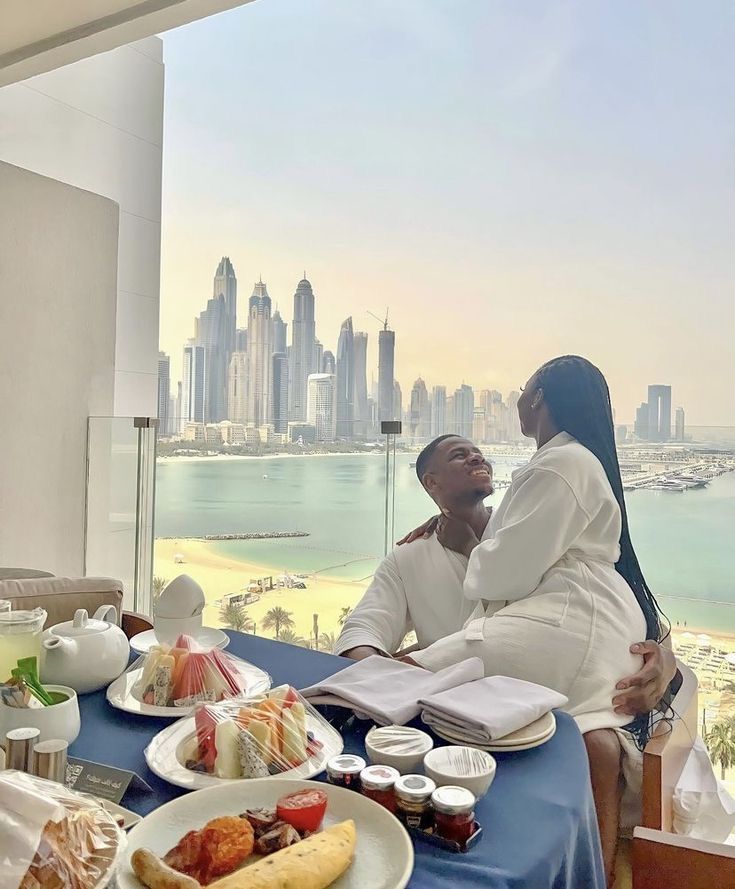 two people sitting at a table with food and drinks in front of the city skyline