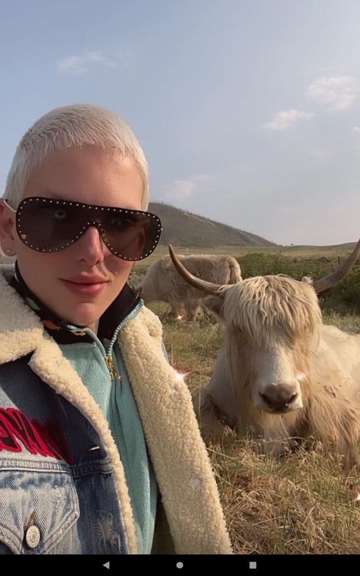 a man with white hair and sunglasses standing next to a cow