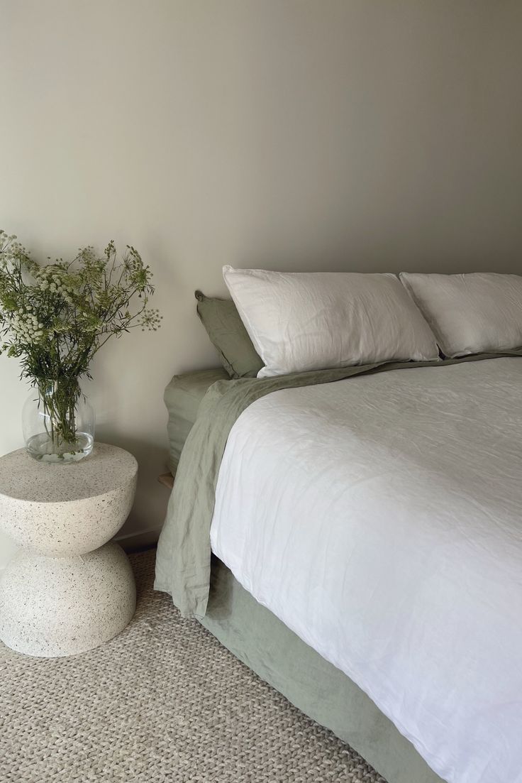 a white bed sitting next to a vase filled with flowers