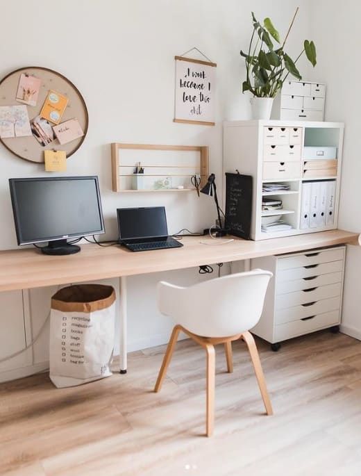 a desk with two computers on it and a plant in the corner next to it