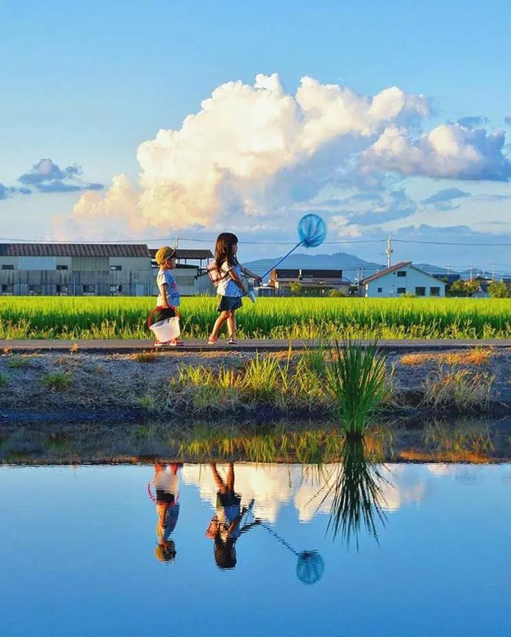 two children are playing near the water with their kites in the sky above them